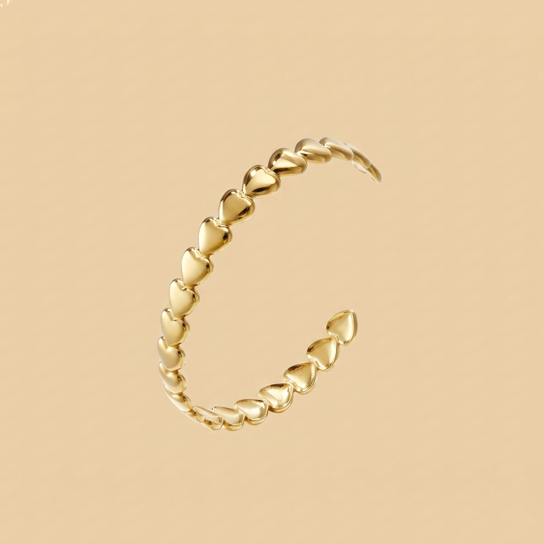 A gold open cuff bracelet featuring a continuous row of small heart-shaped links, displayed on a solid beige background.